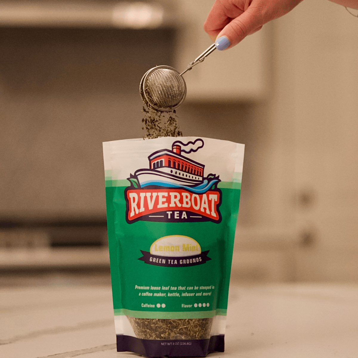 Person pouring tea from a bag labeled 'Riverboat Tea' into a infuser.