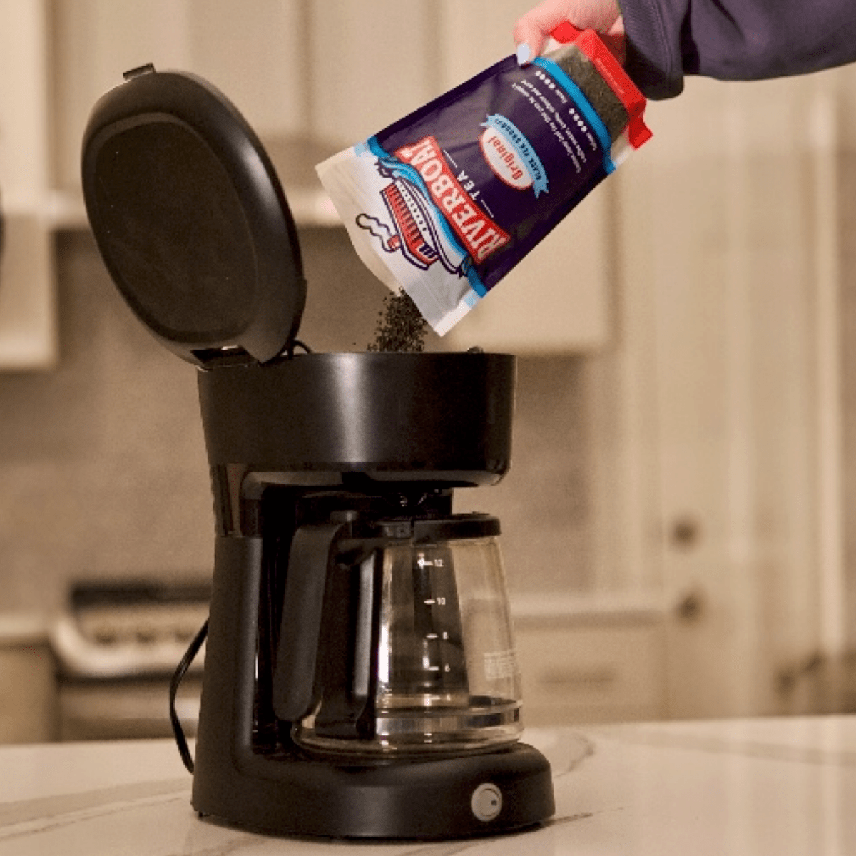 Person adding coffee grounds to a black coffee maker in a kitchen setting.